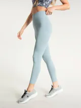 Calza deportiva de tiro alto con largo hasta el tobillo, confeccionada en tejido elástico de color celeste. Presenta un diseño minimalista con costura en V en la cintura y logo pequeño en la cadera.