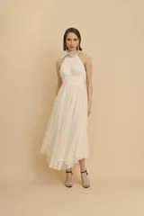 Vestido midi de fiesta color crudo, con cuello halter, cuerpo drapeado y falda de microtul plisado.