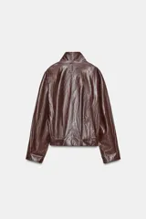 Chaqueta de corte amplio estilo biker en tejido efecto piel de color verde oscuro, con cuello alto envolvente, cierre frontal asimétrico de cremallera metálica, bolsillos ocultos en costura y forro interior.