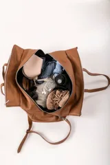 Bolso de viaje tipo weekender de cuero color marrón con doble asa de mano y correa bandolera ajustable y desmontable.