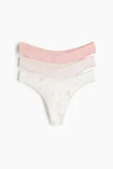 Pack de tres bombachas tipo thong de algodón con tiro bajo, bordes elásticos con detalle de encaje y refuerzo interior. Incluye una de color rosa, una beige y una blanca con estampado floreado.