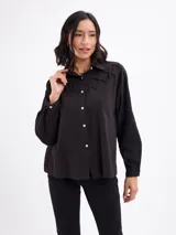Camisa blanca de algodón, de manga larga, con detalle de tiras cruzadas en el canesú delantero y cierre frontal con botones.