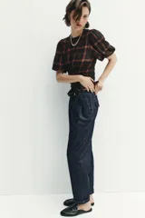 Pantalón chino de tiro medio confeccionado en denim oscuro. Presenta pinzas en el delantero, bolsillos laterales y bajo con acabado en vuelta. Cierre frontal con cremallera y botón.