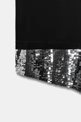 Camiseta negra de corte oversize, cuello redondo y manga corta. Presenta un bajo asimétrico con una aplicación de lentejuelas plateadas a contraste.