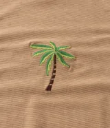 Remera de algodón texturizado color camel, con cuello redondo, manga corta con bajo plegado y un pequeño bordado de palmera en el pecho.