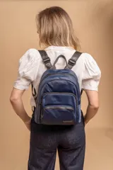 Mochila urbana de diseño funcional en color beige, confeccionada en tela impermeable. Cuenta con un compartimento principal amplio, un bolsillo secundario y un bolsillo frontal, todos con cierre. Incluye asa superior y correas ajustables para los hombros, con detalle de etiqueta de marca en el frente.