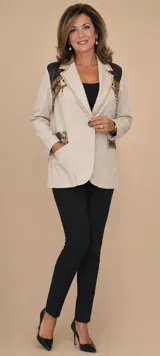 Blazer de gamuza color tostado con diseño artesanal. Presenta flecos en las solapas y bolsillos, bordados florales en los hombros con detalles de perlas colgantes y aplicaciones decorativas en los bolsillos.