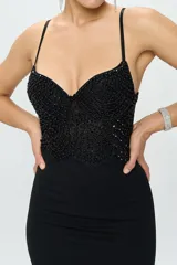 Vestido largo de fiesta color negro, con cuerpo tipo corset estructurado adornado con lentejuelas y perlas, escote corazón y breteles finos. La falda es de corte sirena, entallada en la cintura y caderas, con caída fluida hasta el suelo.