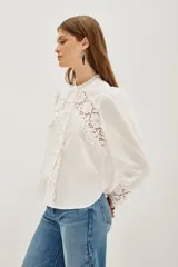 Camisa negra de algodón con detalles de encaje calado en el pecho, hombros y puños. Presenta cuello alto con terminación de encaje, cierre frontal con botones y mangas largas abullonadas.