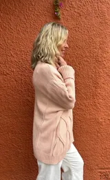 Polera de tejido de punto con diseño de ochos, color rosa viejo, de corte oversize y cuello alto, con mangas largas y puños acanalados.