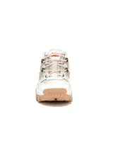 Sneaker Cat modelo Reactor, de diseño robusto y estilo industrial. Presenta una combinación de colores blanco, beige y suela color arena. Cuenta con una estructura de jaula lateral, cordones jaspeados y suela de goma dentada para mayor tracción.