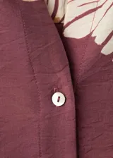 Camisa de manga larga color marrón con estampado floral grande en tonos beige y blanco, cuello camisero y cierre frontal con botones.