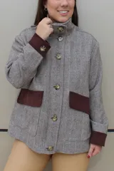 Campera de paño de lana en color beige jaspeado, con diseño oversize. Presenta detalles en pana color marrón chocolate en los puños y en las tapas de los bolsillos frontales. Cuenta con cierre frontal de botones grandes y cuello alto.