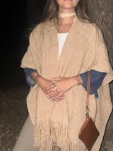 Ruana de lana merino en color champagne, con diseño de tejido de punto y terminación de flecos en el ruedo. Prenda de estilo bohemio y atemporal.