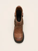 Bota de punta cuadrada realizada en cuero encerado color marrón, con hebillas en la caña, herrajes de níquel y fondo de suela negro.