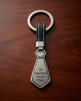 Llavero de acero con diseño en forma de corbata y grabado con la frase 'Te queremos mucho Papá'. Incluye una correa de cuero sintético y una argolla metálica circular.