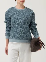 Buzo de algodón orgánico con cuello redondo y mangas largas. Presenta un diseño estampado con motivos florales y paisley en técnica flock sobre fondo gris.