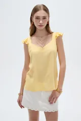 Musculosa amarilla de viscosa, con cuello en V y breteles anchos decorados con volados. Presenta un corte holgado.
