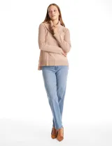 Buzo de punto color beige con cuello volcado amplio, mangas largas acanaladas y torso liso. Presenta una costura central vertical, ruedo con tajos laterales y largo asimétrico, siendo más largo en la parte posterior.