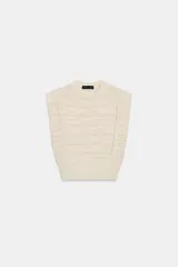 Jersey de punto color crema, sin mangas (manga sisa) con hombreras marcadas y cuello redondo. Presenta textura de tejido con líneas horizontales en relieve.
