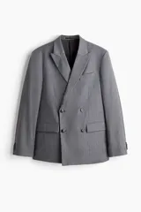 Blazer cruzado de color gris medio, con solapas de pico, ojal decorativo y cierre de doble botonadura. Presenta bolsillo superior insertado, bolsillos delanteros ribeteados con solapa y botones decorativos en los puños.