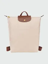 Mochila de diseño minimalista en color beige, con solapa y asa superior en cuero marrón texturizado. Cuenta con correas ajustables en color marrón y cierre principal.
