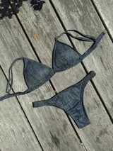 Conjunto de bikini con efecto denim, compuesto por un top de triángulo fijo con breteles regulables y cierre de gancho en la espalda, y una bombacha tipo vedetina con laterales fruncidos.