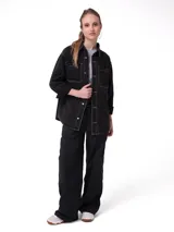 Camisa oversize de denim negro con costuras en contraste color blanco, bolsillos dobles en el pecho con solapa, cierre frontal de botones metálicos y dobladillo redondeado.