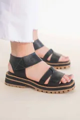 Sandalias de cuero negras con tiras cruzadas y ajuste al tobillo. Suela track color caramelo.