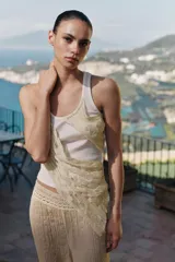 Top de cuello redondo y sin mangas, confeccionado en tejido de punto acanalado color crema. Presenta una aplicación asimétrica de tela tipo georgette en tono beige claro que cruza el frente de la prenda.