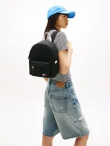 Mochila compacta Tommy Jeans color negro, con diseño curvo, compartimento principal con cierre de cremallera, bolsillo exterior con cremallera y parche con el logo de la marca en la parte delantera. Cuenta con correas ajustables y acolchadas.