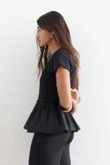 Top negro de manga corta y cuello redondo. La parte superior es de tejido liso y ajustado, mientras que la parte inferior es un bajo globo con textura plisada y semitransparente.