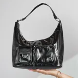 Cartera tipo hobo de cuero sintético color negro, con correa corta al hombro y dos bolsillos frontales con cierre.