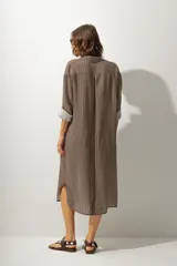 Vestido camisero midi de corte recto y holgado, con estampado de rayas verticales en tonos tierra, cuello camisero, cierre frontal de botones y mangas tres cuartos con puños vueltos.