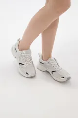 Zapatilla deportiva de estilo urbano en color blanco con detalles metalizados plateados y acentos en negro. Presenta una combinación de malla transpirable y paneles sintéticos, con suela robusta y cordones al tono.