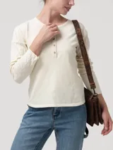 Remera de manga larga en color blanco hueso, con cuello redondo y cierre frontal parcial con botones. Presenta un diseño de tejido trenzado con textura en las mangas y cuerpo liso.