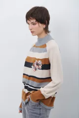 Polera de tejido de punto con diseño de rayas horizontales en tonos beige, marrón, gris y negro. Presenta cuello redondo y mangas largas con puños en contraste.