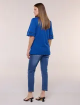 Remera de algodón azul con escote redondo y pequeña abertura central en V. Cuenta con mangas de largo intermedio decoradas con una inserción horizontal de puntilla calada y tajos laterales en el ruedo.