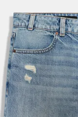 Jeans de tiro bajo, corte recto y pierna ancha, color celeste claro desgastado. Presenta roturas visibles en la zona de la rodilla y pequeños desgastes en los muslos y bolsillos.
