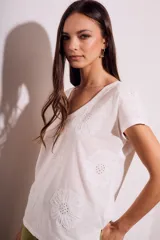 Remera de algodón color blanco con cuello en V y mangas cortas. Presenta un diseño con flores bordadas en relieve y detalles calados en el tejido.