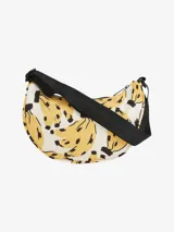 Bolso tipo bandolera con estampado de bananas amarillas y negras sobre fondo blanco. Tiene correa negra ajustable y cierre superior con cremallera.
