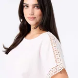 Camiseta blanca de manga corta holgada, con detalles de bordado y macramé en las mangas y cuello redondo.