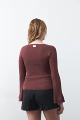 Top de tejido acanalado negro, con escote en V, mangas largas con terminación acampanada y ajuste al cuerpo.