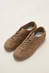 Zapatillas de estilo urbano color chocolate, confeccionadas en material textil tipo gamuza, con cordones al tono y suela de goma plana.