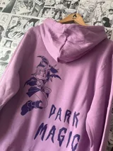 Canguro lila con capucha y cordones, con estampado circular en el frente con símbolos y letras. Diseño inspirado en el personaje Maga Oscura del anime Yu-Gi-Oh!.