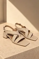 Sandalias de cuero vacuno color beige, con diseño de tiras cruzadas en el empeine, puntera cuadrada, taco bloque mediano y tira ajustable con hebilla en el talón.