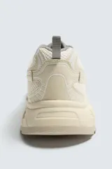 Zapatilla deportiva estilo running con diseño de paneles superpuestos en malla y material sintético. Presenta cordones curvados y una suela robusta con volumen y diseño irregular.