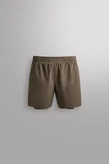 Short de running 2 en 1 color beige, confeccionado en tejido técnico ligero y elástico con malla interior integrada. Presenta cintura elástica ajustable con cordón, bolsillo trasero con cierre y aberturas laterales en el bajo.