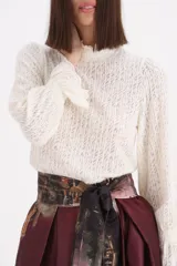 Sweater de punto calado en color crudo, con cuello alto tipo polera y mangas largas con puños con volados.