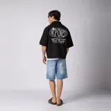 Camisa de manga corta color marfil, corte boxy, con cuello camisero, cierre frontal de botones y pequeño bordado marrón en el pecho con las siglas VCP.